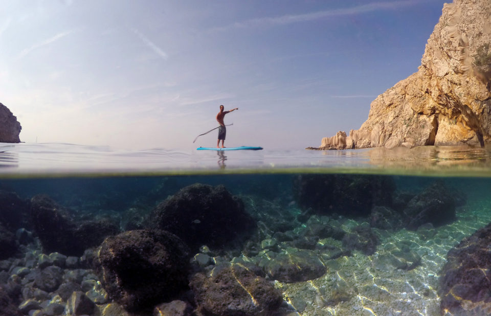 Stand up paddler paddling over underwater landscapes split photo