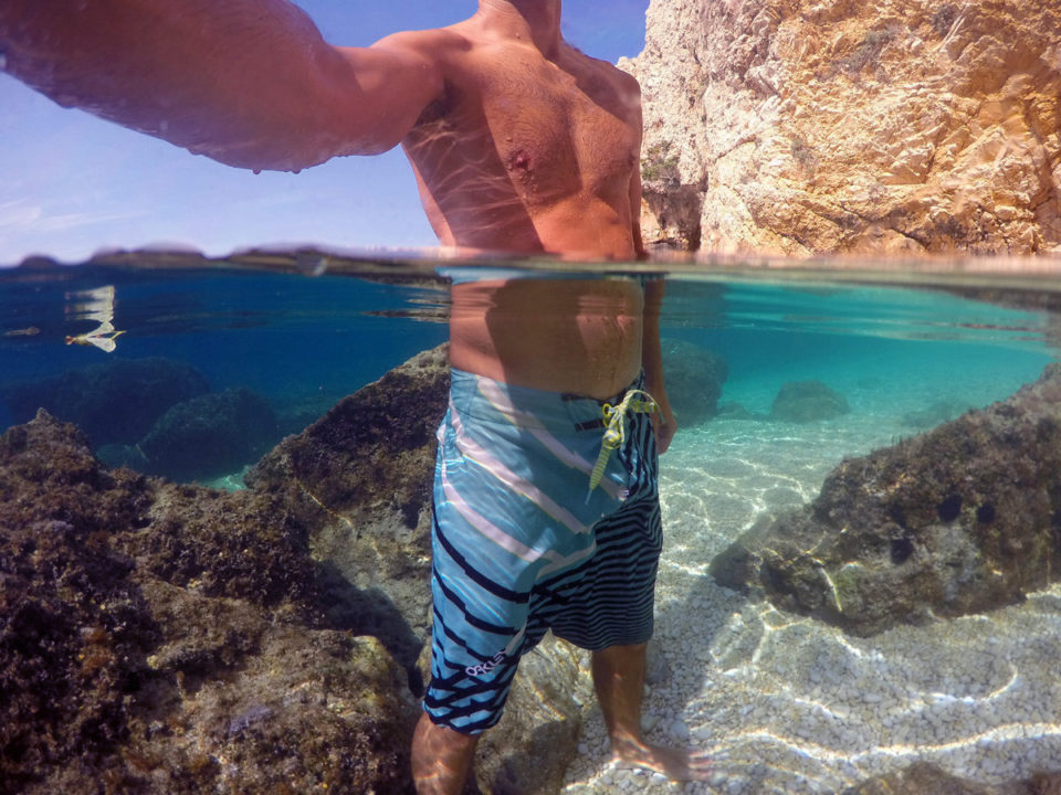 Man in boardshorts standing in water half half photo